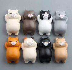 small plastic cat figurines sitting in a row on a gray surface with white and black cats behind them