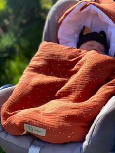 an orange blanket on top of a baby in a car seat