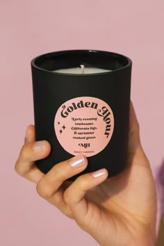 a woman's hand holding a black candle in front of a pink background with the words golden glow on it