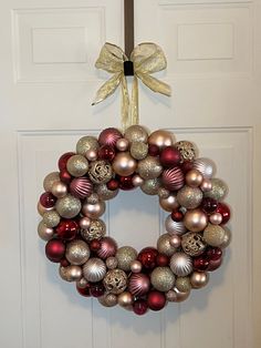 a christmas wreath hanging on the front door with ornaments around it and a bow tied to it