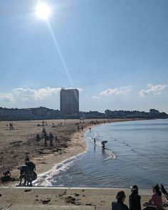 people are sitting and standing on the beach by the water while others play in the water