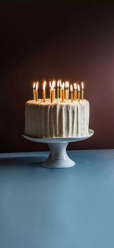 a white cake with lit candles on it sitting on a blue countertop in front of a dark background