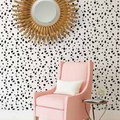 a pink chair sitting in front of a wall with black and white dots on it