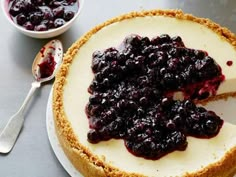 a cheesecake with blueberry topping on a plate next to a bowl of fruit