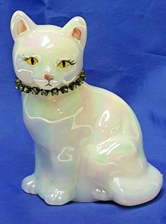 a white cat figurine sitting on top of a blue surface with a chain around it's neck