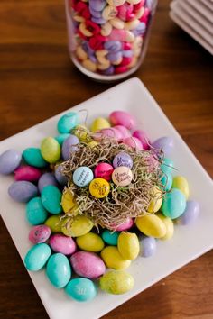 a white plate topped with lots of colorful candy eggs and small nest on top of it