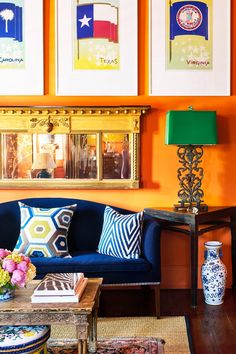 a living room with orange walls, blue couches and colorful paintings on the wall