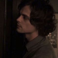 a man with curly hair standing in front of a door and looking off into the distance