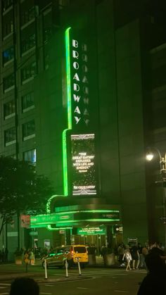 people are standing on the street in front of a building that is lit up with green lights