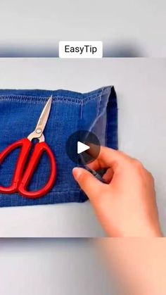 someone is using scissors to sew on a pair of blue jean pants with red handles