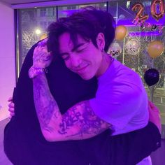 a man with tattoos hugging another man in front of balloons