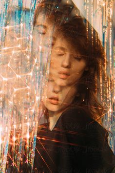 a man with long hair standing in front of a window covered in lights and strings