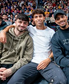 three men sitting next to each other in front of a crowd at a basketball game