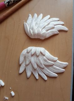 two pieces of white clay sitting on top of a wooden table next to a pencil