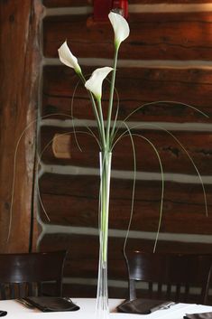 there is a tall vase with flowers in it on the dining room table, ready to be used as a centerpiece