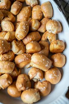 a white bowl filled with bread rolls covered in sesame seeds and sprinkled with sesame seeds