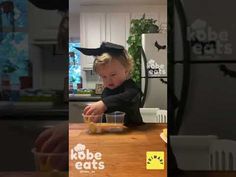 a toddler sitting at a table with food in front of him and the caption reads, kobe eats