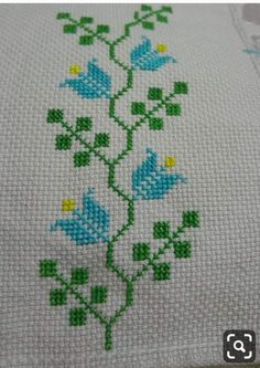 a cross stitch pattern with blue flowers and green leaves on white fabric, in the shape of a flower