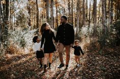 an adult and two children are walking through the woods with leaves on the ground in front of them