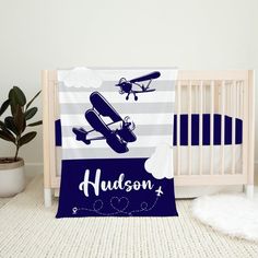 a baby crib with a blue and white blanket that says hudson next to an airplane