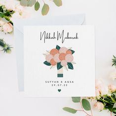 a white card with pink flowers on it and greenery next to the envelope that says,