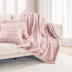 a white couch with pink pillows on top of it and a blanket draped over the back