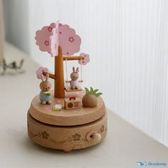 a wooden clock with two rabbits on it's sides and a pink umbrella in the background