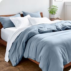 a bed with blue sheets and pillows in a white room next to a potted plant