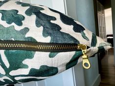 a green and white camouflage print pillow with gold zippers on the front, along with a pair of scissors