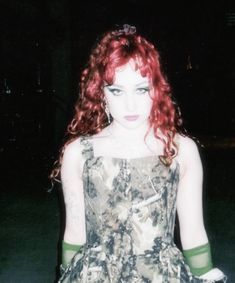 a woman with red hair wearing a dress and green gloves on her hands, standing in the dark