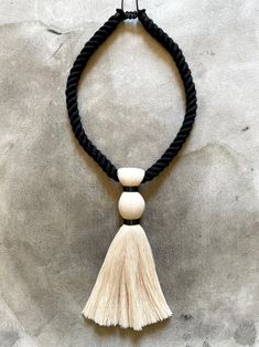 a white tasseled necklace hanging on a black cord with a wooden bead