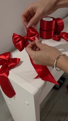 a woman is wrapping red ribbon on a white box