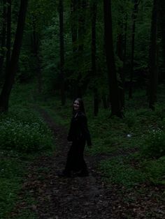 a woman walking down a path in the woods at night with her hair blowing back