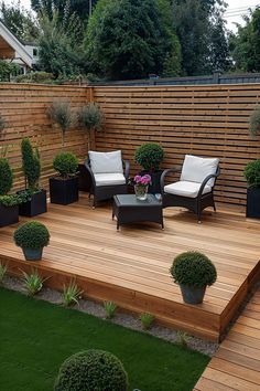 a wooden deck surrounded by potted plants and lawn furniture with white cushions on it