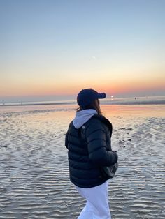 a person standing on the beach at sunset with their back to the camera, looking out into the water