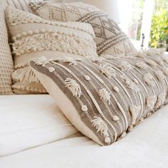 a close up of pillows on a bed with white linens and pom poms