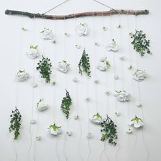 white flowers and greenery are hanging on a wall next to a branch with branches