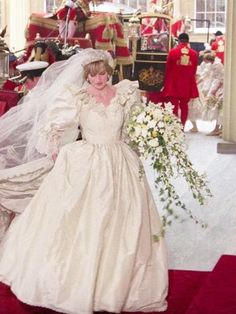 a woman in a white wedding dress and veil walking down the aisle with her bouquet