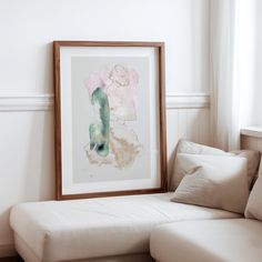 a white couch sitting next to a window in a living room under a framed painting