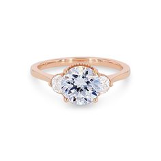 a rose gold engagement ring with three diamonds on the band and an oval center stone