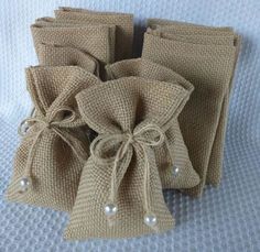 four bags with pearls on them sitting on a bed together, tied in burlap