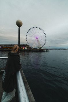 a person sitting on a pier looking at the ferris wheel