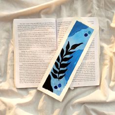 an open book with blue and black designs on the pages next to it is laying on a white sheet