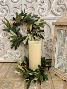 a white candle sitting on top of a wooden table next to a mirror and wreath