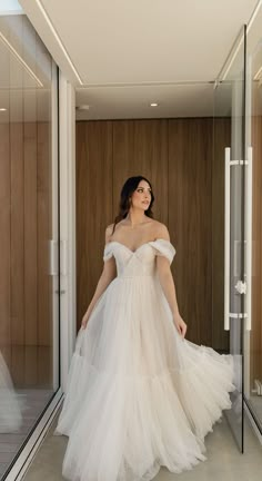 a woman in a white dress is standing by a glass wall and looking into the distance