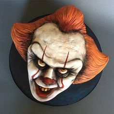 a creepy clown mask on top of a black plate with red hair and orange eyes