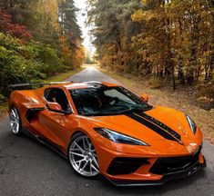 an orange sports car parked on the side of a road in front of some trees