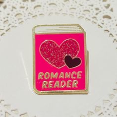 a pink enamel pin with a heart and the words romance reader on it