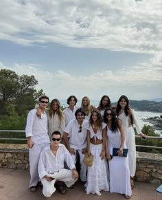 a group of people standing next to each other on top of a stone wall near the ocean