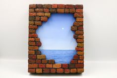 a brick wall with a hole in the middle that has water and sky on it